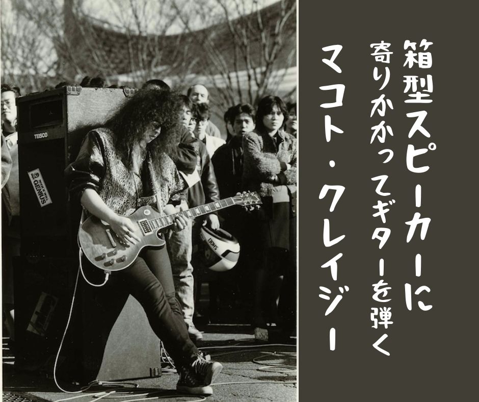 A man leaning on a box speaker and playing the guitar